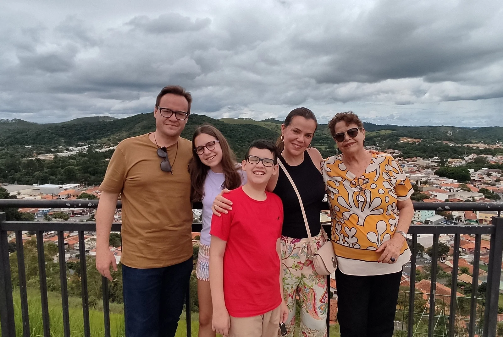 Tiago Augusto com família em mirante com vista de paisagem montanhosa e cidade ao fundo